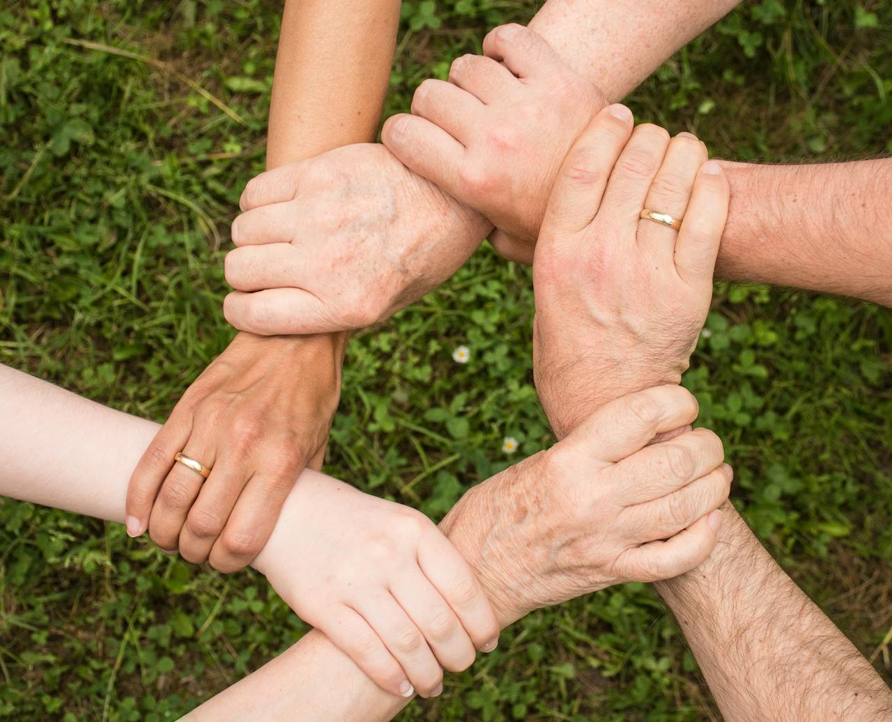 about-us-01 Close-up of diverse hands forming a connection, symbolizing teamwork and unity outdoors.