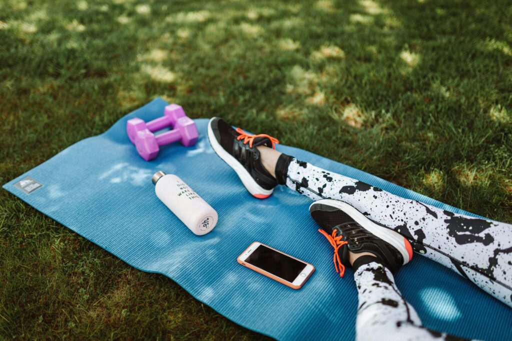 Focused workout setup outdoors with mat, dumbbells, phone, and water bottle.